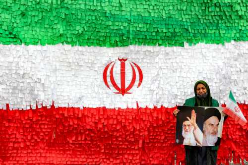A woman poses with the pictures of Iran's late and current supreme leaders, Ayatollah Ruhollah Khomeini and Ayatollah Ali Khamenei, as she stands before an installation depicting the Iranian flag, during a rally marking the 47th anniversary of the 1979 Islamic revolution, in Tehran on February 11, 2026.