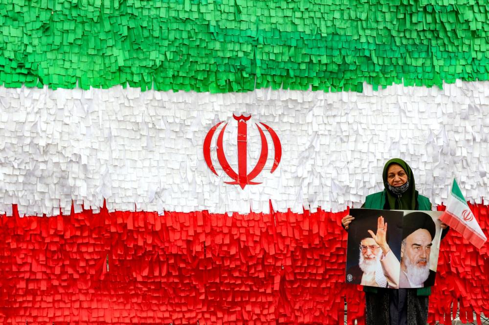 A woman poses with the pictures of Iran's late and current supreme leaders, Ayatollah Ruhollah Khomeini and Ayatollah Ali Khamenei, as she stands before an installation depicting the Iranian flag, during a rally marking the 47th anniversary of the 1979 Islamic revolution, in Tehran on February 11, 2026.