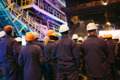 Workers in hard hats and protective clothing stand near heavy machinery