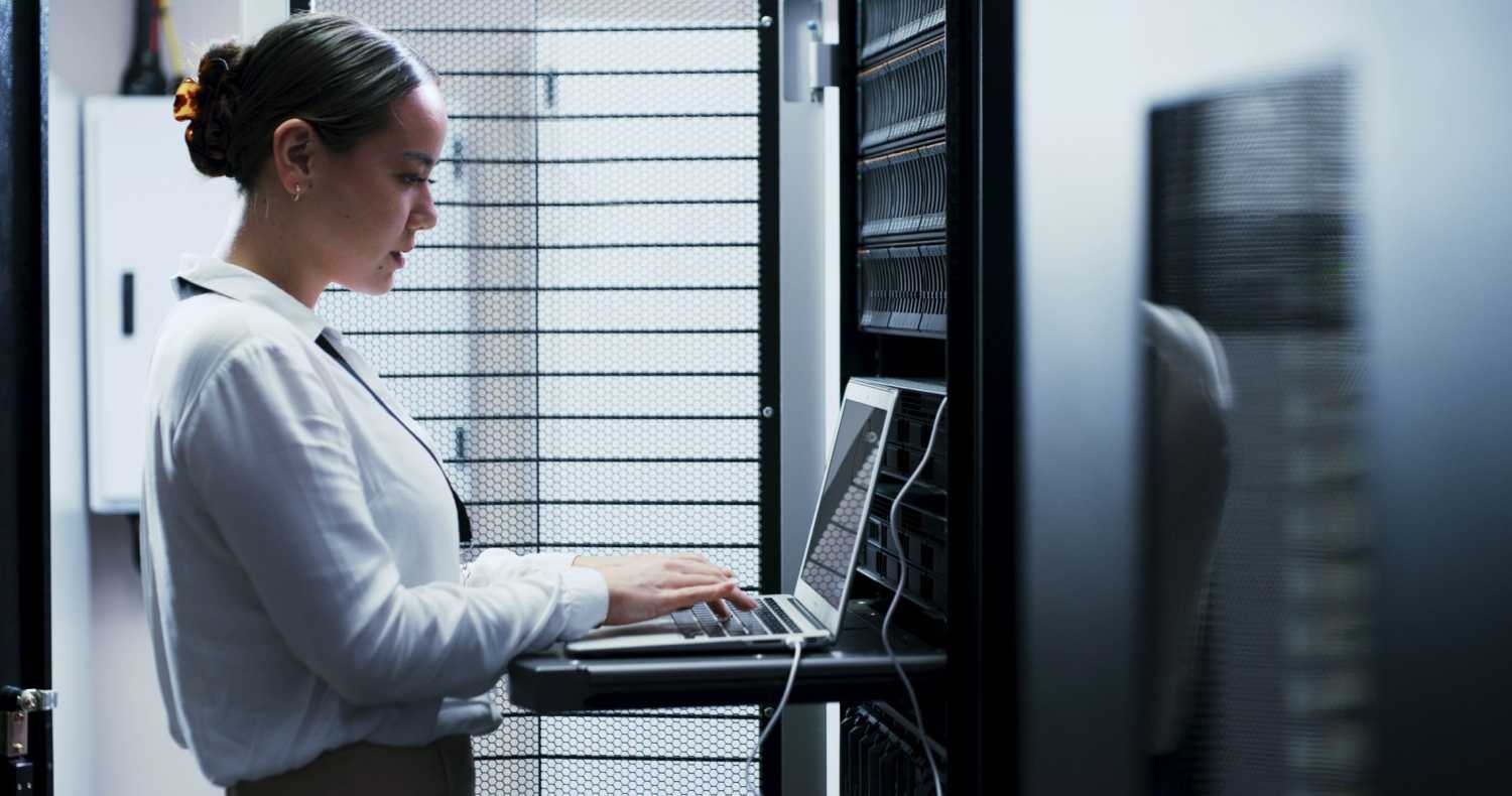 A woman works at a laptop connected to a server