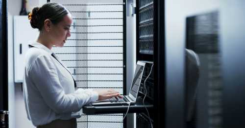 A woman works at a laptop connected to a server