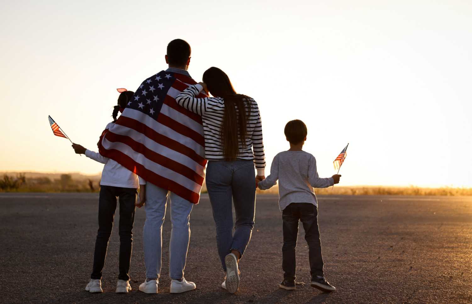 A family with American flags in a sunset landscape.