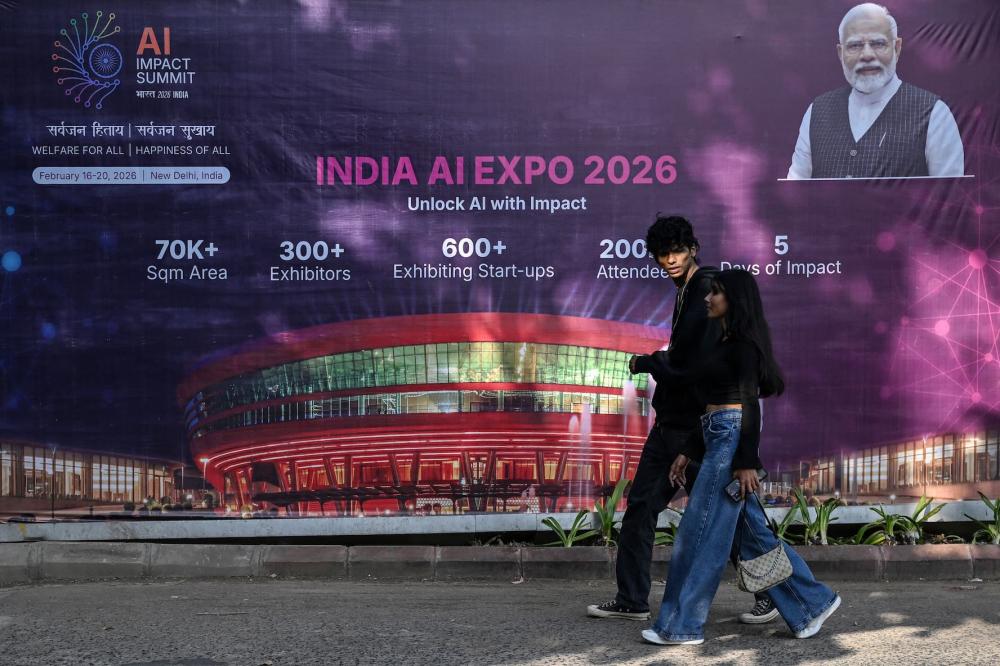 Commuters walk past a hoarding of the AI Expo along a street on the eve of the 'India AI Impact Summit 2026' in New Delhi on February 15, 2026.