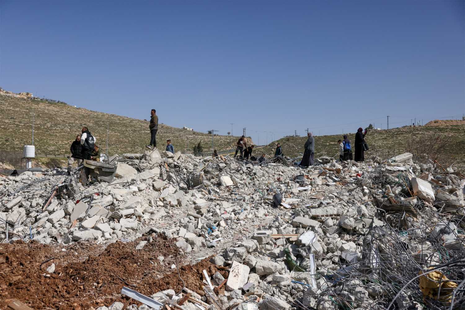 Members of the Salhab family on the rubble of their apartment building after it was demolished by Israeli bulldozers near the Israeli settlement of Hagai, south of the occupied West Bank city of Hebron, on February 18, 2026.
