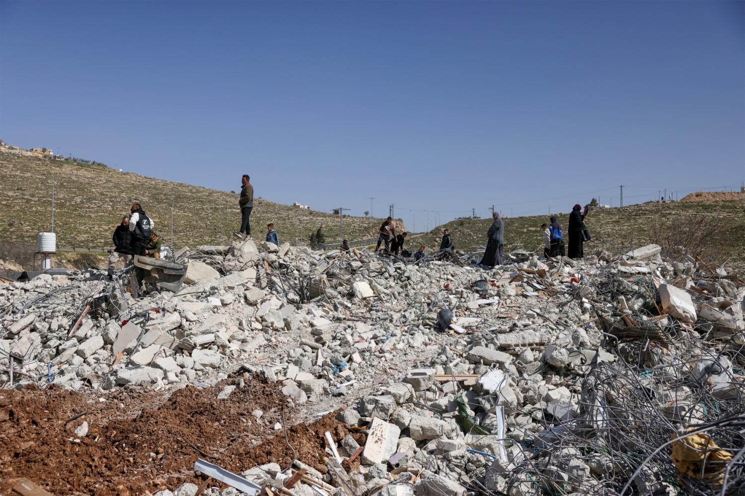 Members of the Salhab family on the rubble of their apartment building after it was demolished by Israeli bulldozers near the Israeli settlement of Hagai, south of the occupied West Bank city of Hebron, on February 18, 2026.