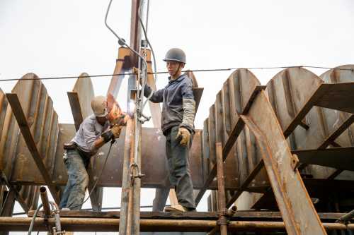 China, Chongqing, Workmen assembling steel plates into ship's hull at sprawling Chongqing Dongfeng Shipyard on autumn morning.