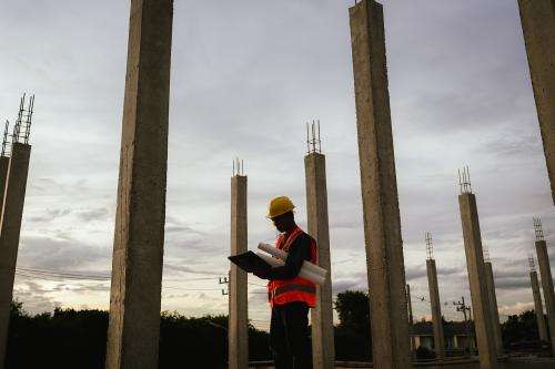 Silhouette of a construction worker holding blueprints and using a phone at a building site during sunset, symbolizing planning, progress, and evening work on-site.