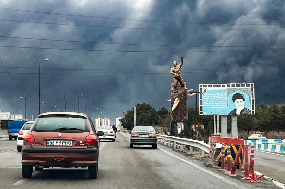 Cars move along a highway past a war memorial statue and a billboard depicting Iran's late supreme leader, Ayatollah Ali Khamenei, in Tehran, March 8, 2026. (Photo by AFP via Getty Images)