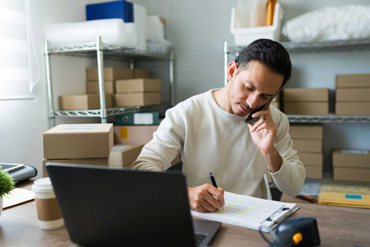 Latin entrepreneur taking notes while talking on the phone with a customer and managing orders in his small business store