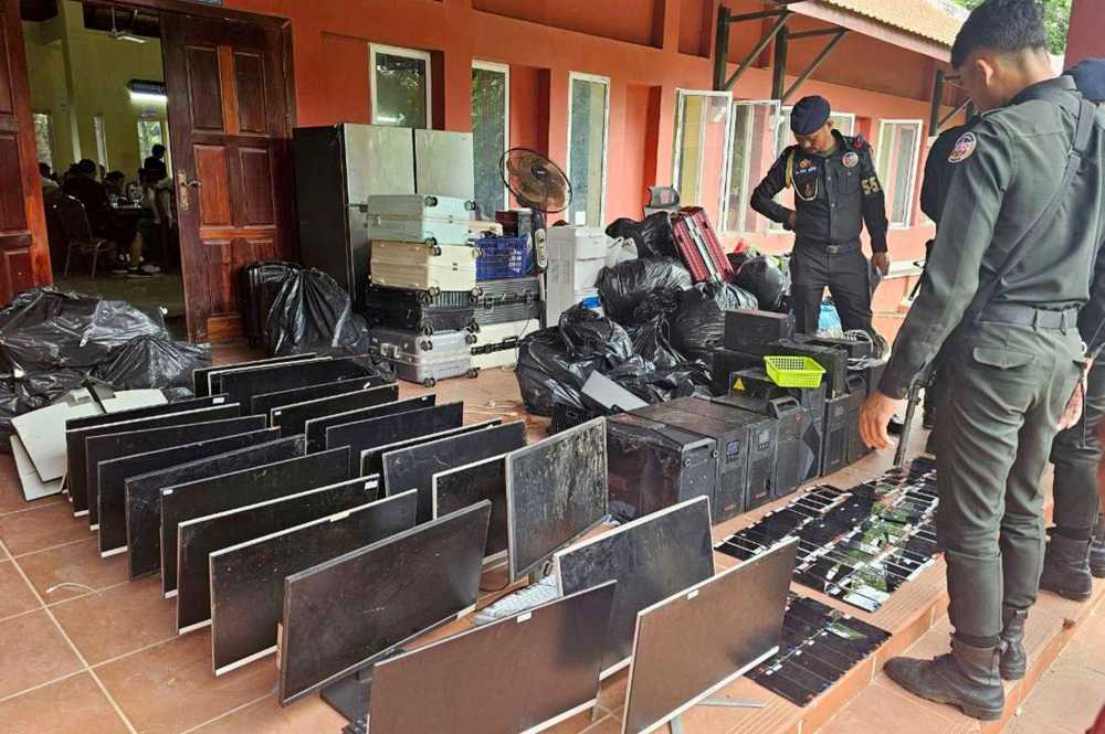 This pool photo taken on July 17, 2025 and released on July 18 by Agence Kampuchea Presse (AKP) shows military police looking at computers, smartphones and other equipment seized during a raid on a scam centre in Kandal province.