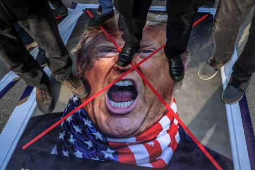 Protestors stand on an image depicting US President Donald Trump during a gathering to protest against the US and Israel attack of Iran and the killing of the Supreme leader in front of the US Embassy in Ankara on March 1, 2026.
