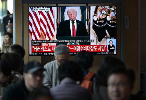 People watch a television screen showing a live broadcast of US President Donald Trump delivering national address on war against Iran, at a train station in Seoul on April 2, 2026.