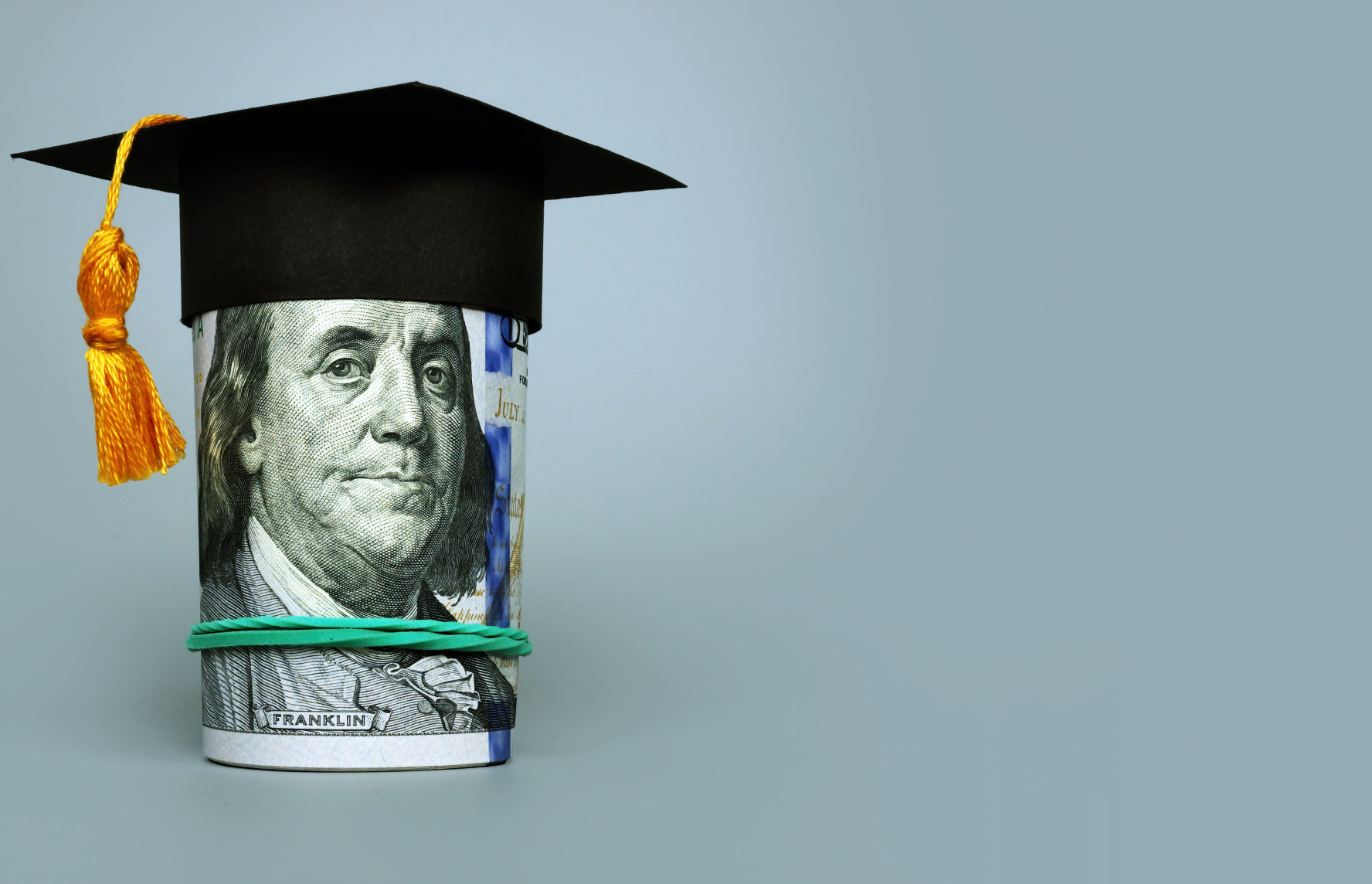 A rolled up hundred dollar bill wearing a black college graduation cap