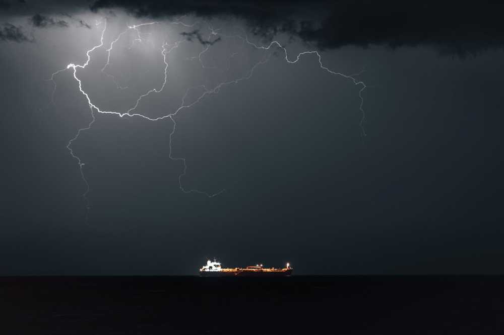 An oil tanker sails as lightning strikes overhead