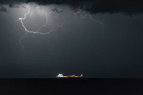 An oil tanker sails as lightning strikes overhead