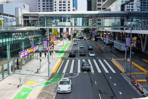 Cars drive past Moscone Center North Hall under a skybridge, surrounded by GDC, Game Developers Conference banners and green bike lanes - San Francisco, California, USA - March 15, 2025