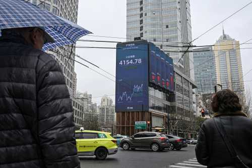 Pedestrians walk past a screen showing the Shanghai composite index in the Jing'an district of Shanghai on March 2, 2026.