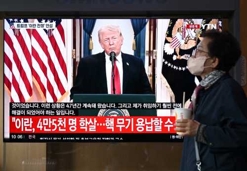 A woman walks past a television screen showing a live broadcast of US President Donald Trump delivering national address on war against Iran, at a train station in Seoul on April 2, 2026.