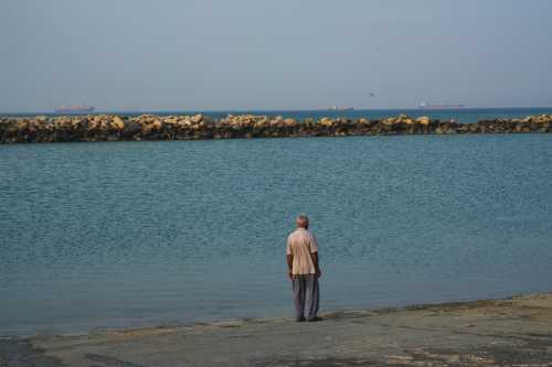A man walks the shoreline as boats navigate the sea on April 28, 2026 on Qeshm Island, Iran in the Strait of Hormuz.