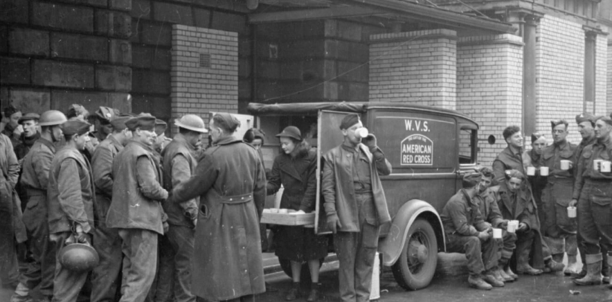 Patience 'Boo' Brand and Rachel Bingham serve tea to men of the Royal Engineers from the back of a WVS tea car, donated to the WVS by the American Red Cross.