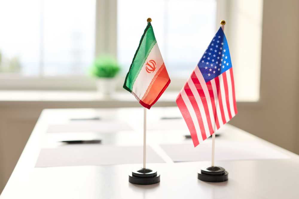 The Iranian and American flags are depicted on a table symbolizing negotiations.