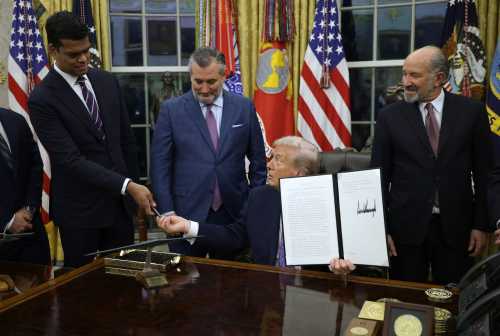 WASHINGTON, DC - DECEMBER 11: U.S. President Donald Trump hands a pen to Senior White House Policy Advisor on Artificial Intelligence Sriram Krishnan after signing an executive order while U.S. Sen. Ted Cruz (R-Texas) and Commerce Secretary Howard Lutnick look on in the Oval Office of the White House on Dec. 11, 2025, in Washington, DC.