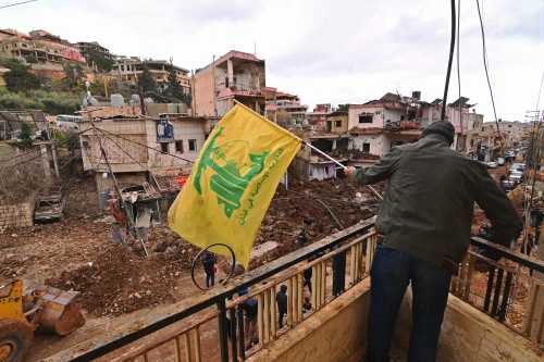 This photograph taken during a media tour organised by the Hezbollah shows a man installing a flag of Hezbollah on the balcony of a damaged building at Nabi Sheet town after an Israeli military operation in the Bekaa Valley of Lebanon, on March 7, 2026.