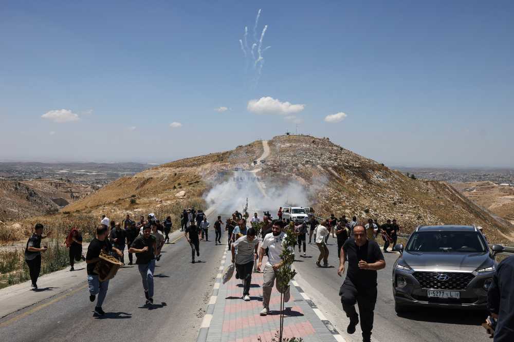 Protesters and local Palestinian landowners, who say some of their land was taken for the newly built Mount Tarousa settlement (background), run from tear gas fired by Israeli security forces blocking a road leading to the hilltop during a rally against the settlement near Dura in the Israeli-occupied West Bank on June 19, 2026.