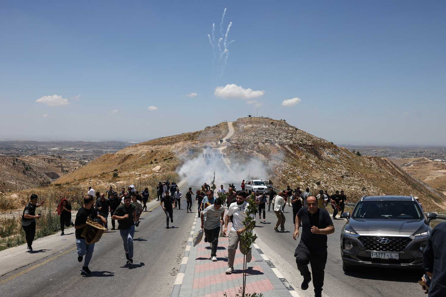 Protesters and local Palestinian landowners, who say some of their land was taken for the newly built Mount Tarousa settlement (background), run from tear gas fired by Israeli security forces blocking a road leading to the hilltop during a rally against the settlement near Dura in the Israeli-occupied West Bank on June 19, 2026.