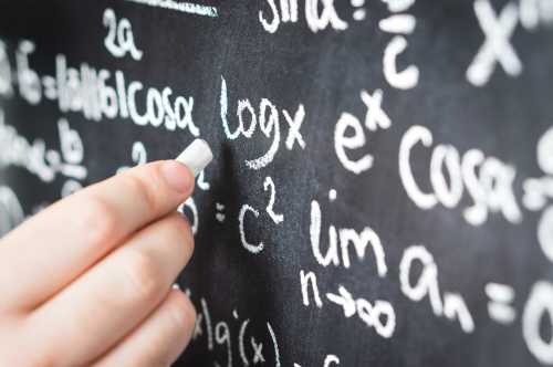 Professor writing mathematical formula and equation to blackboard in school classroom.