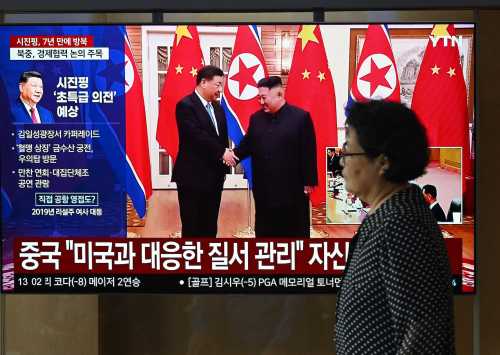 A woman walks past a television screen showing a news broadcast with file footage of the 2019 meeting between China's President Xi Jinping and North Korean leader Kim Jong Un, at a train station in Seoul on June 8, 2026.