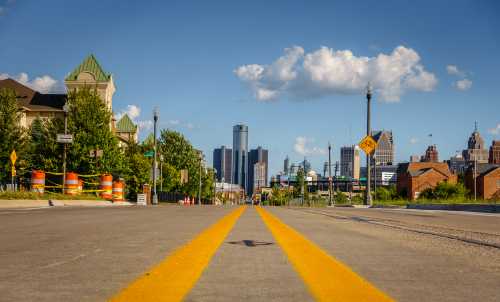 An empty street through an old Detroit city neighborhood with downtown buildings in the background.