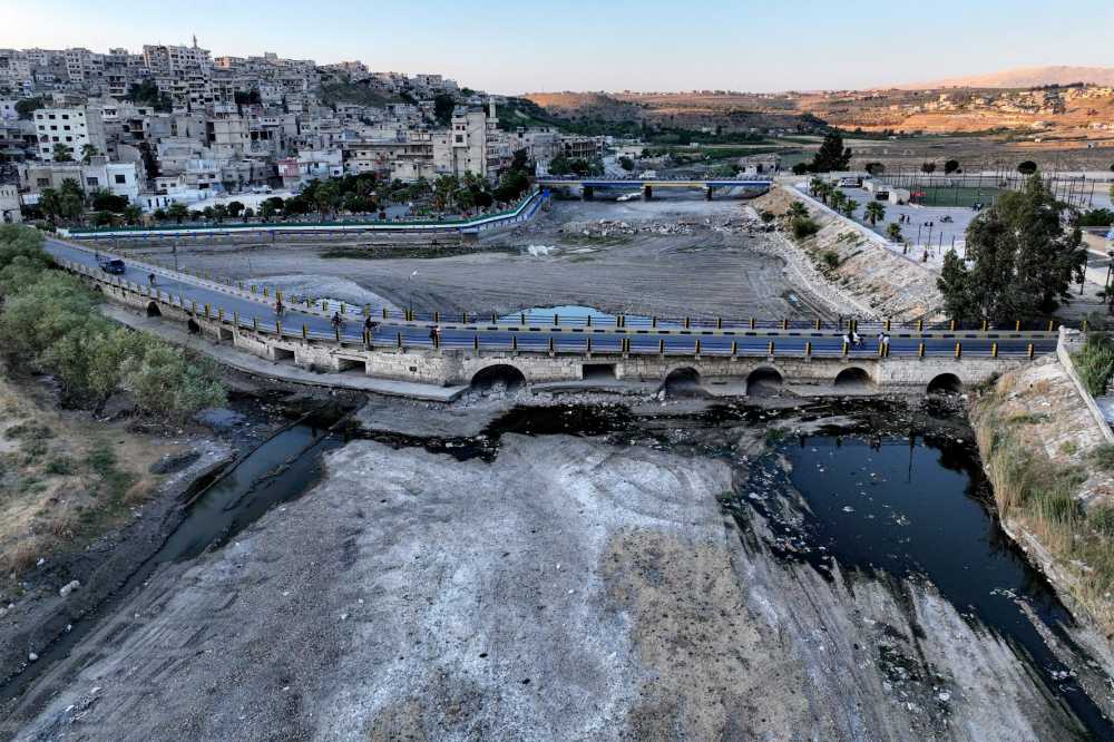 This aerial view shows patches of water by a bridge in the mostly-dry riverbed of Syria's Orontes (Assi) river during an extreme drought in the city of Jisr al-Shughur in Syria's northwestern Idlib province on August 4, 2025.