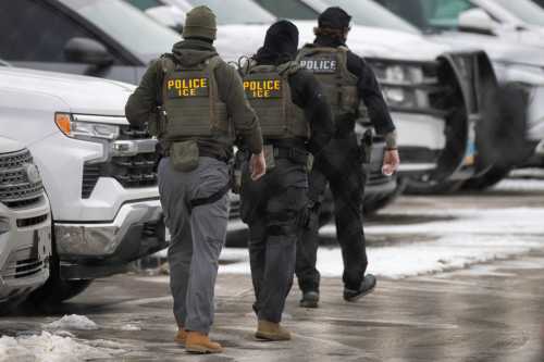 Three men dressed in protective vests marked "Police ICE" walk through a snowy parking lot.