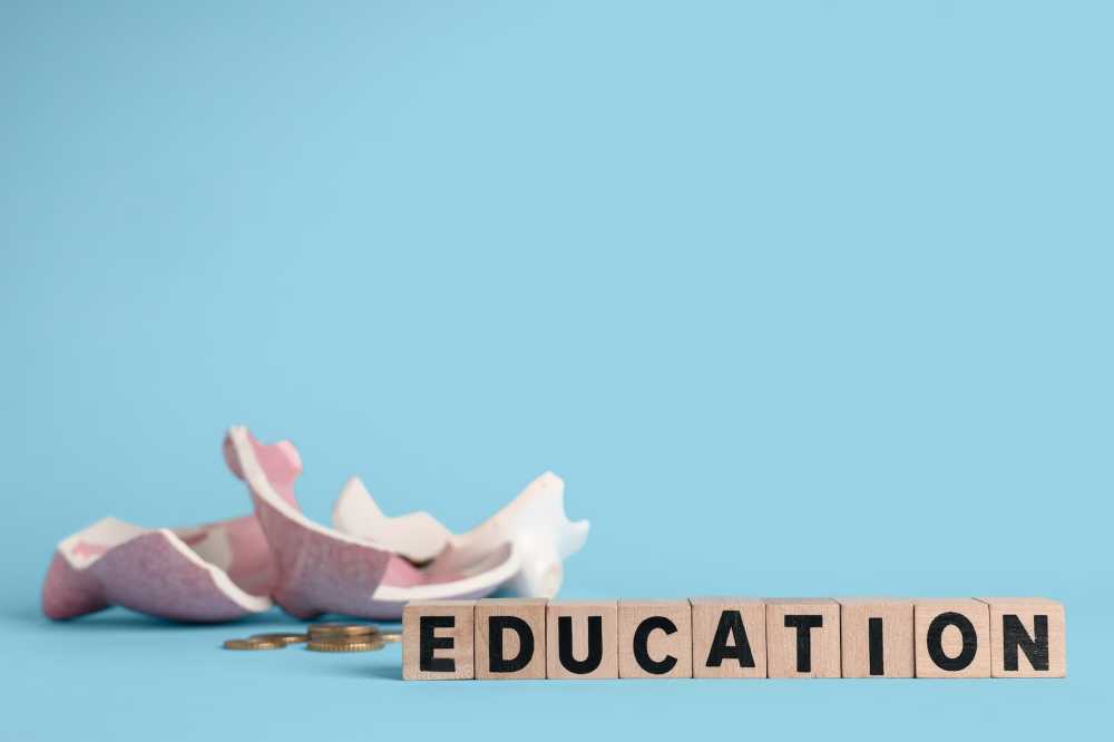 Broken piggy bank with coins and word EDUCATION on blue background